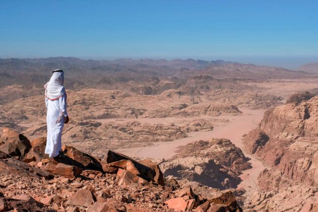 A bedouin standing in the summit Jabal Umm ad Dami, the highest mountain in Jordan. Panoramic landscape of the valleys and hills in the remote region of Jordan, near to the border with Saudi Arabia.
